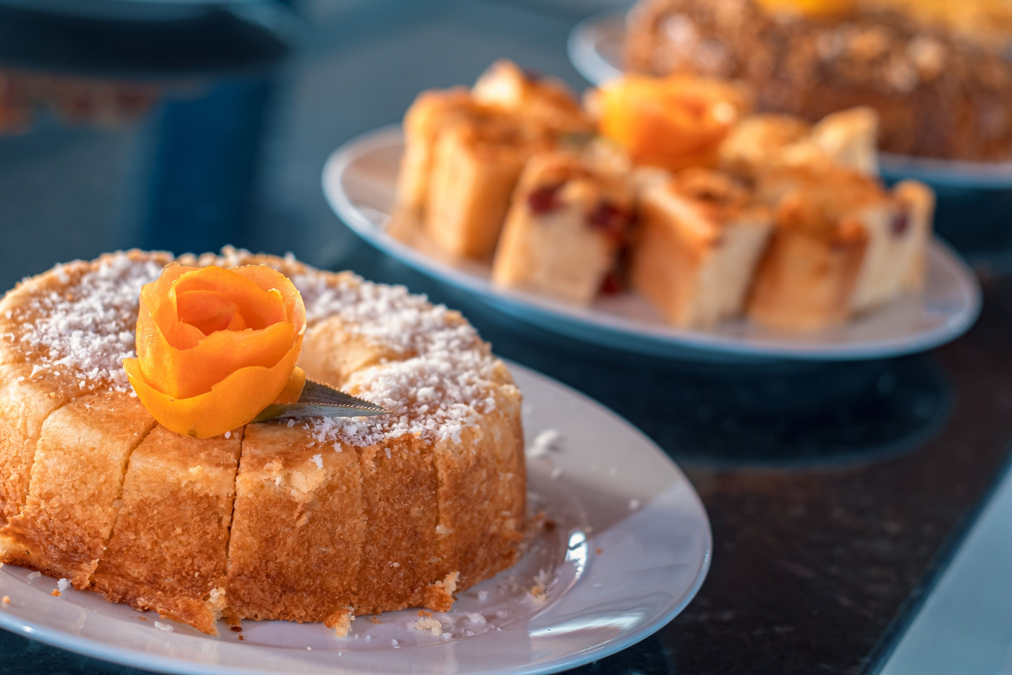 A dessert table with a variety of cakes and pastries, including a bundt cake with a decorative orange flower on top.