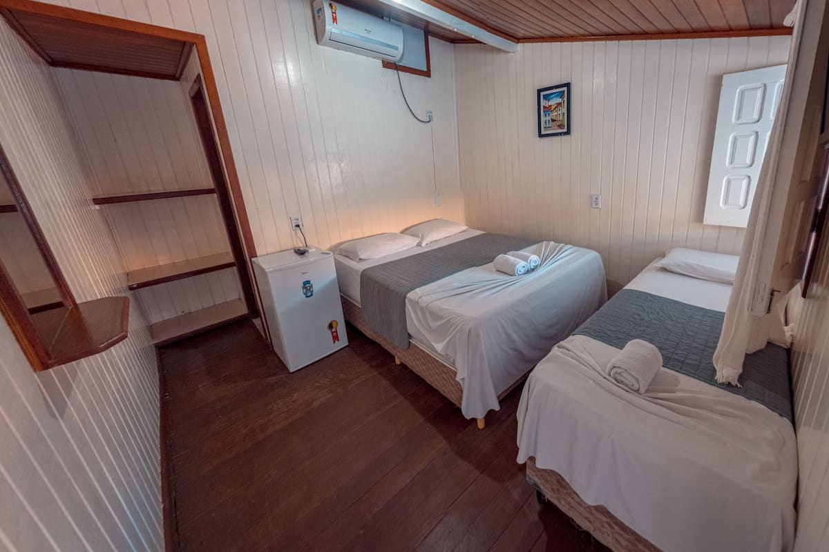 A room with two beds, a small white refrigerator, and a ceiling fan.
