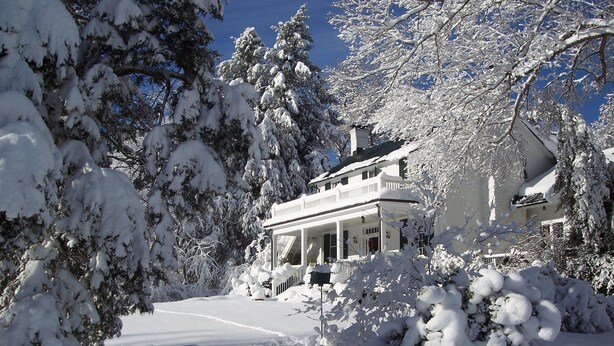 A snow-covered house with a porch and a clear blue sky. - Inn at Monticello (Charlottesville)