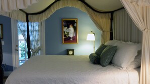 A four-poster canopy bed with a white canopy, a painting on the wall, a bedside lamp, and a clock on the nightstand. - Inn at Monticello (Charlottesville)