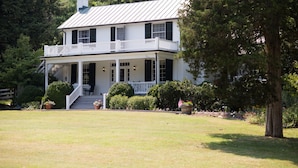 A two-story white house with a balcony, surrounded by a well-maintained lawn and trees. - Inn at Monticello (Charlottesville)
