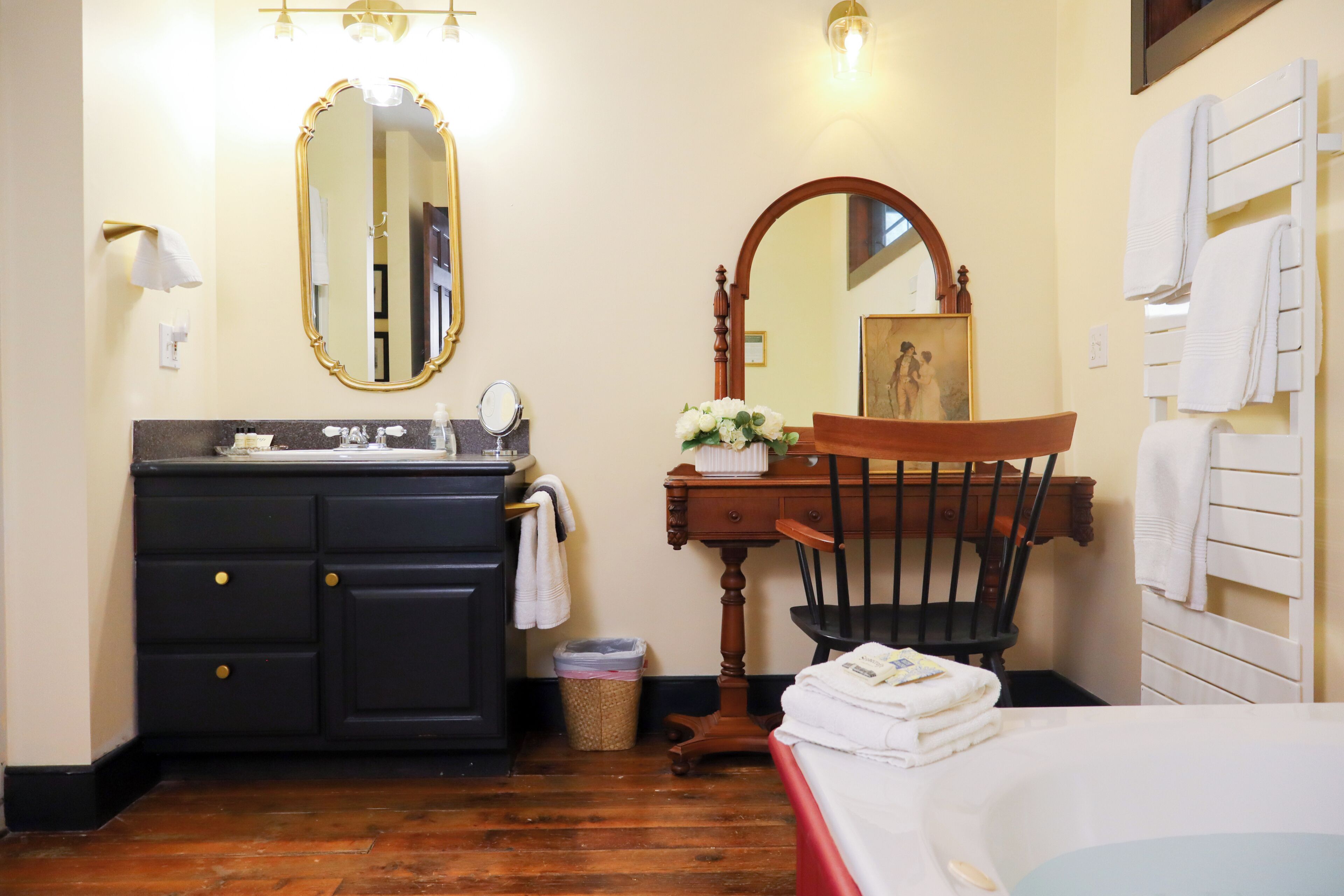 A bathroom with a wooden vanity, a large mirror, a chair, and a bathtub.