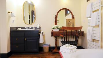 A bathroom with a wooden vanity, a large mirror, a chair, and a bathtub.