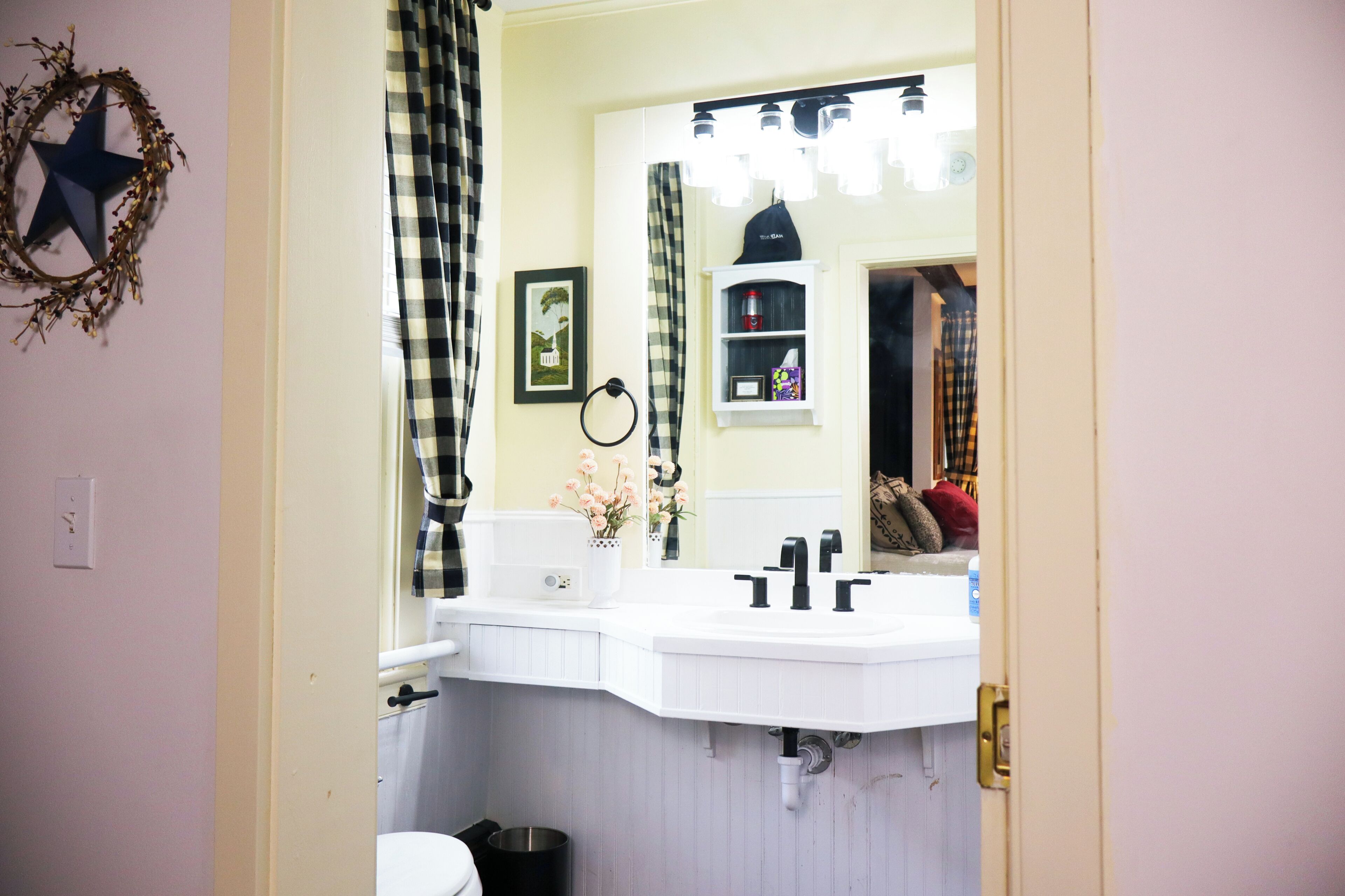 A bathroom with a white sink, a mirror, a star decoration, and a checkered curtain.