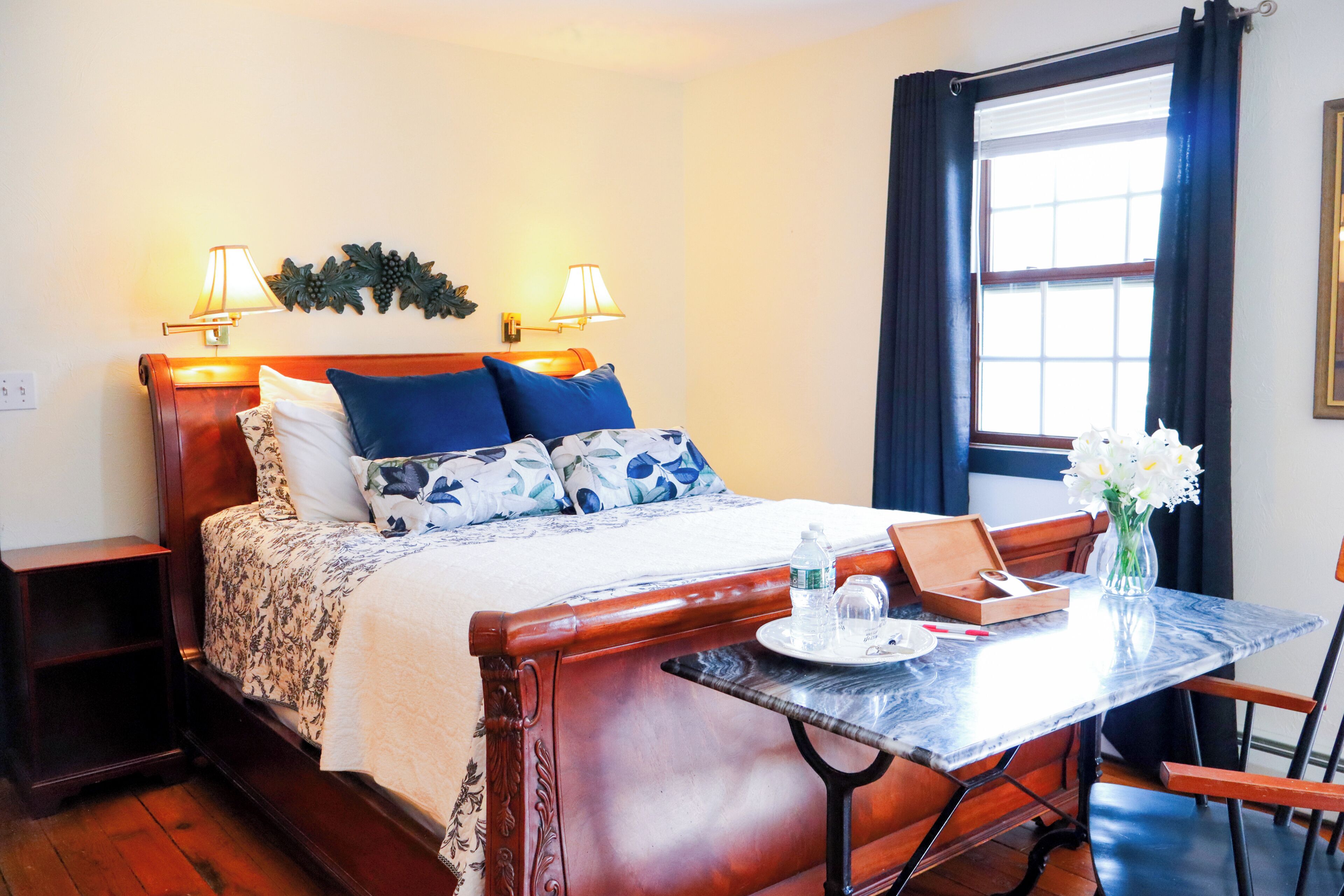 A neatly arranged hotel room with a bed, bedside lamps, a table with a vase, and a window with curtains.