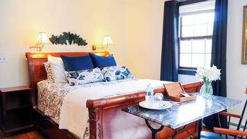 A neatly arranged hotel room with a bed, bedside lamps, a table with a vase, and a window with curtains.