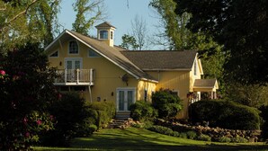 A yellow house with a balcony, a small tower, and a well-maintained garden. - Stonecroft Inn (Ledyard)