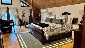 A bedroom with a large bed, wooden flooring, a window with curtains, a chair, a table, and a cabinet. - Stonecroft Inn (Ledyard)