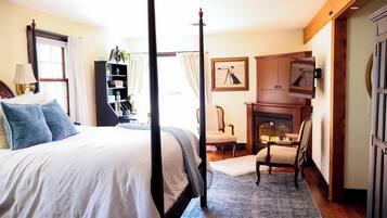 A bedroom with a four-poster bed, a bookshelf, a desk, and a fireplace.
