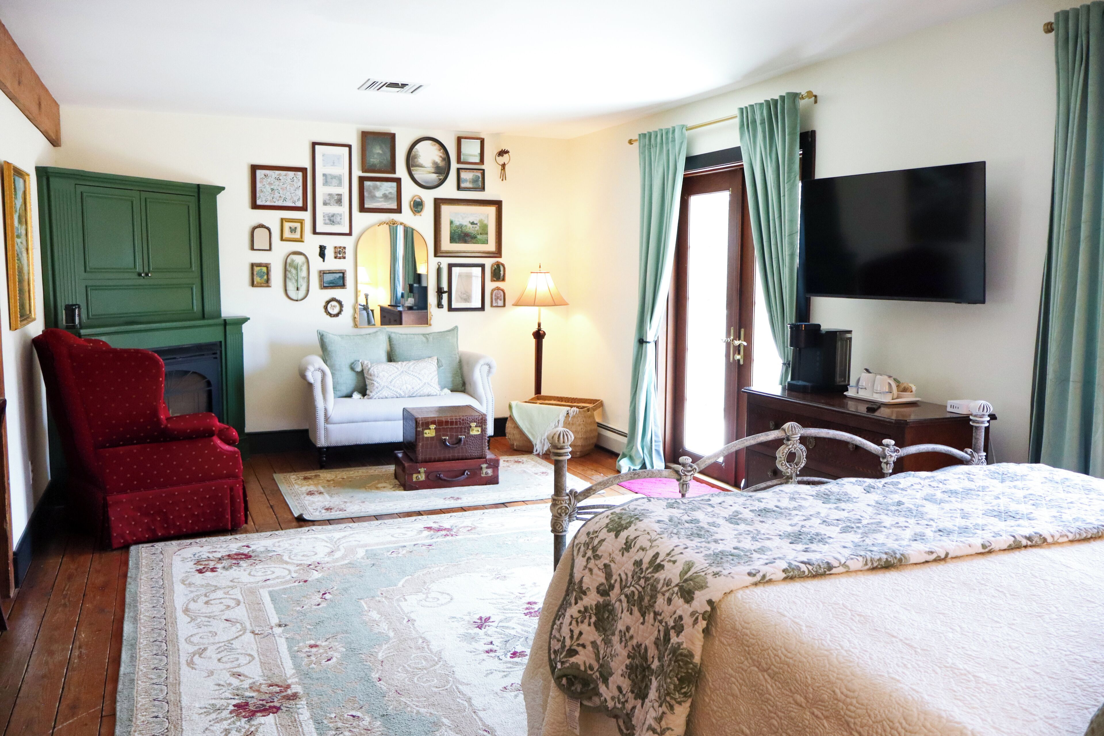 Une chambre à coucher comprenant un lit, un fauteuil rouge, une commode, un téléviseur et un mur décoré de tableaux.