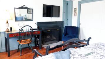 Een kamer met een open haard, een aan de muur bevestigde televisie, een bureau met stoel, en een bed met een beddengoed met een patroon.