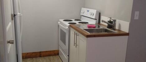 Una cocina compacta con muebles blancos, horno integrado, estufa y una pequeña encimera.