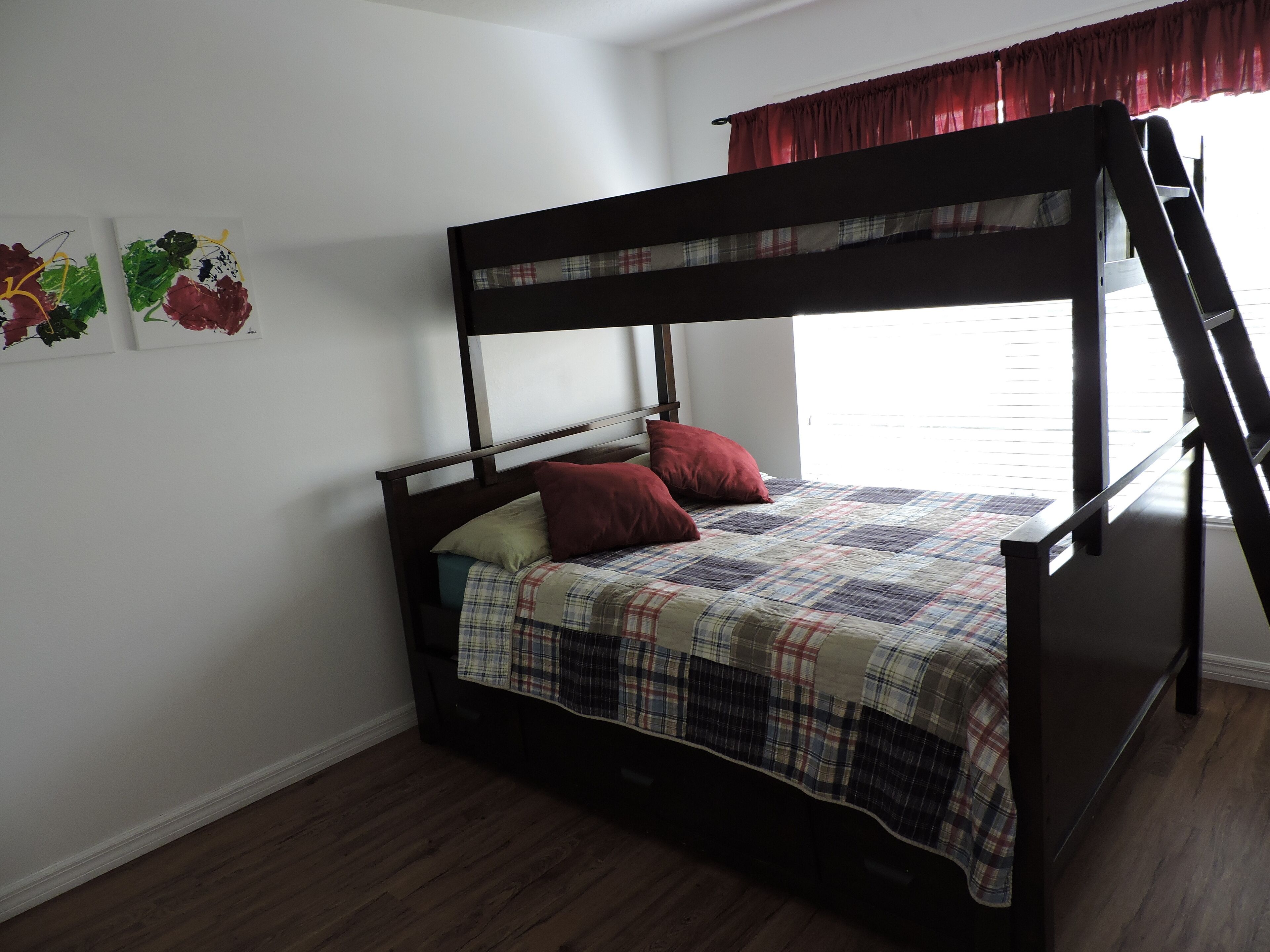 Una cama individual con un edredón escocés y dos almohadas, suelo de madera y una ventana con persianas.