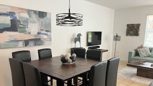A dining area with a dark wooden table, six black chairs, a black chandelier, a painting on the wall, a flat-screen TV, and a sofa with cushions. - BEAUTIFUL LAKEVIEW TOWNHOME, 5 MILES TO DISNEY... FULLY EQUIPED (kissimmee)