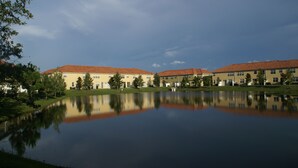 A row of yellow buildings with red roofs reflecting in a calm body of water, surrounded by greenery. - BEAUTIFUL LAKEVIEW TOWNHOME, 5 MILES TO DISNEY... FULLY EQUIPED (kissimmee)