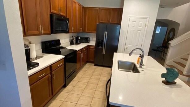 A modern kitchen with wooden cabinets, a black refrigerator, a microwave, and a sink. - BEAUTIFUL LAKEVIEW TOWNHOME, 5 MILES TO DISNEY... FULLY EQUIPED (kissimmee)