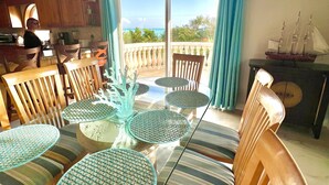A dining area with a round table and chairs, a view of the ocean through a sliding door, and wooden ceiling beams. -  “RENOVATED Gorgeous House with ocean views from balconies, with Hot Tub & Pool” (Marathon)