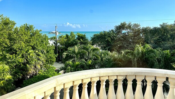 A balcony with a balustrade overlooking a beach and lush greenery. -  “RENOVATED Gorgeous House with ocean views from balconies, with Hot Tub & Pool” (Marathon)