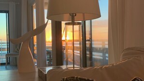 A room with a view of a sunset over a bridge, a lamp, and a patterned pillow on a sofa.
