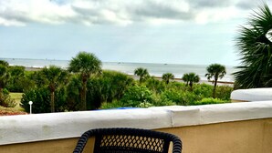 A balcony with a table and chairs overlooking a beach with palm trees and the ocean.