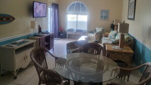 A living room with a glass-top table, wicker chairs, a sofa, and a television.