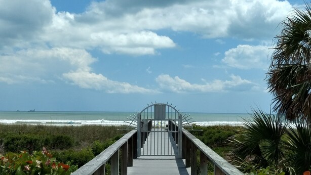 A wooden boardwalk leading to a gated entrance with a view of the ocean and beach.