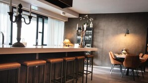 Een moderne bar met een lange toonbank, meerdere barkrukken en een eettafel met stoelen.