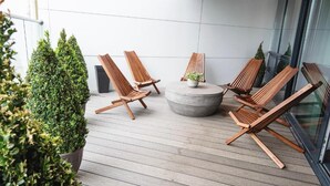 Een houten terras met vier stoelen en een ronde tafel, omringd door potplanten.