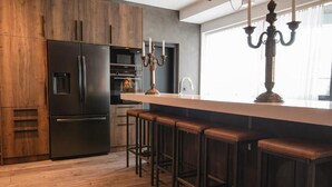 Een moderne keuken met een inbouwkoelkast, een bar met krukken, en een raam met kandelaar.