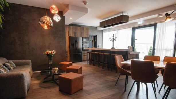 Een moderne woonkamer met een bank, poefs en een eethoek met stoelen en een tafel.