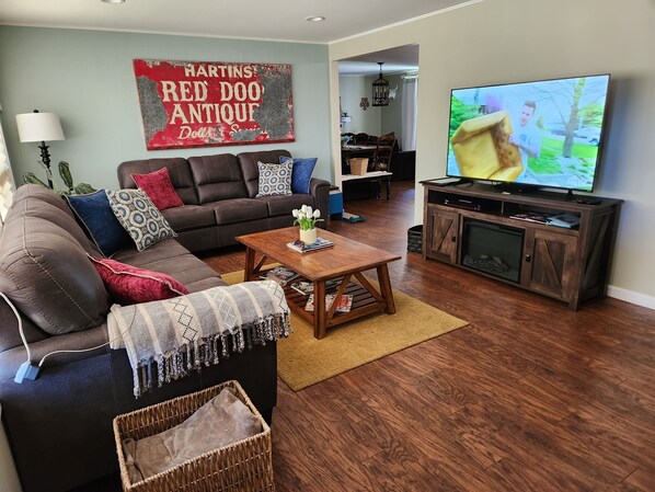A living room with a brown leather sofa, a coffee table, a TV on a wooden stand, and a red sign on the wall.