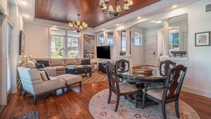 A spacious living room with a wooden ceiling, a large sofa, a dining table with chairs, and a television.