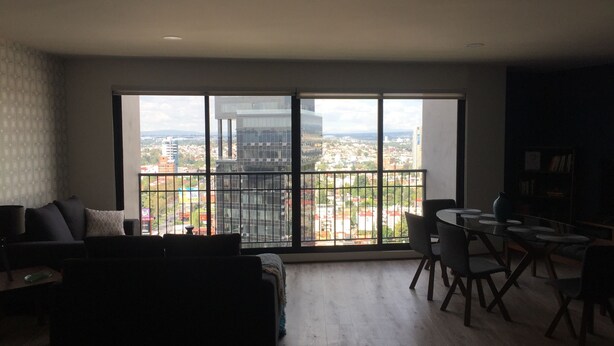 A spacious living room with a large sliding glass door leading to a balcony with a city view.