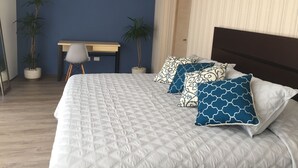 A bedroom with a large bed, a desk, two potted plants, and a chair.