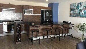 A modern kitchen with a built-in oven, microwave, and refrigerator. There are four bar stools and a large island with a sink.