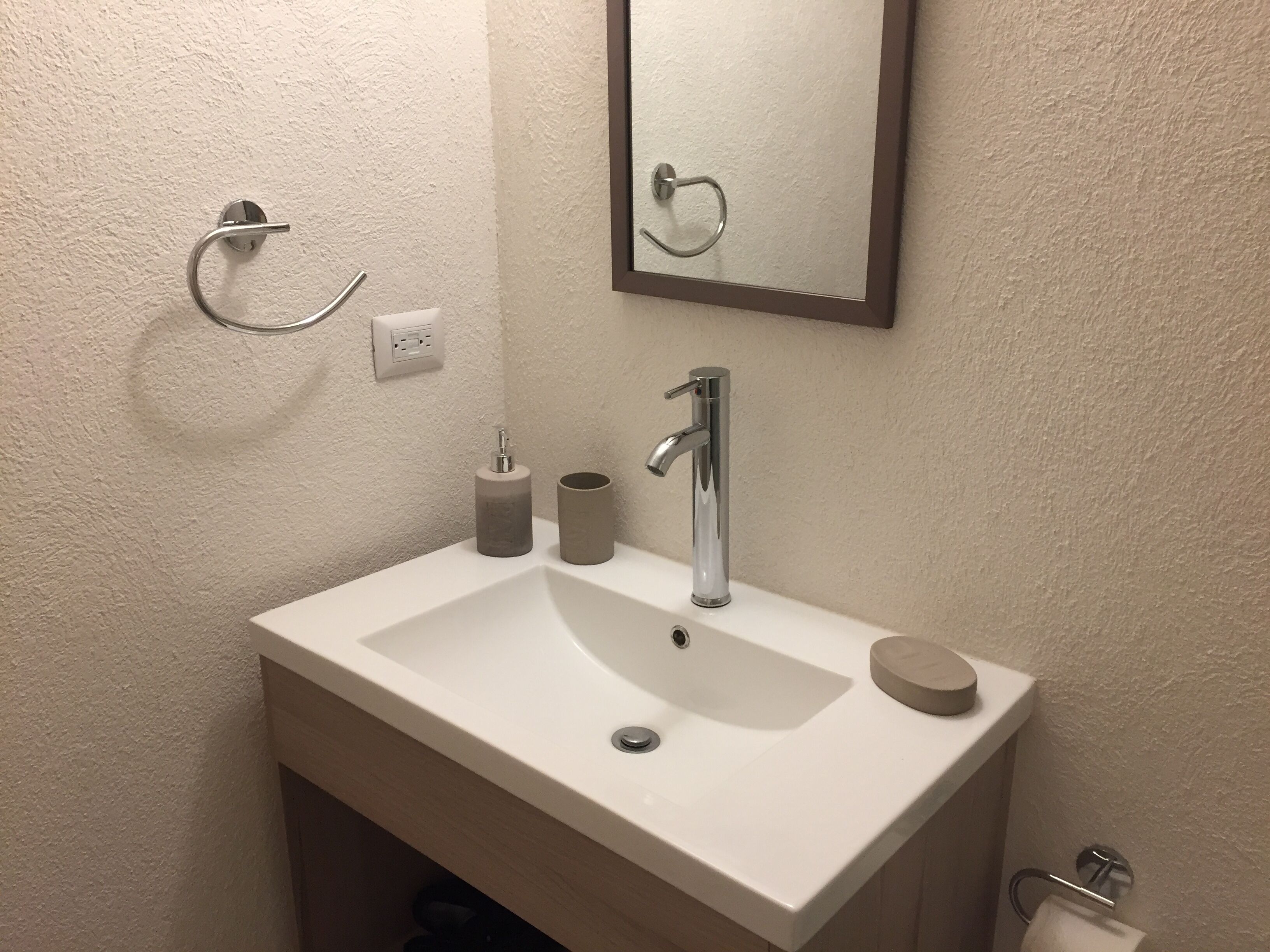 Et badeværelse med en hvid vask, et spejl, et håndklædestativ og en toiletpapirholder.