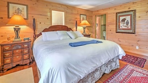 A wooden-paneled bedroom with a large bed, two bedside tables with lamps, and framed pictures on the walls. - 42 acres with Dramatic Mtn. Views...Close to Appalachian Trail (Bakersville)