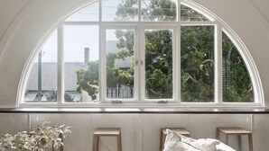 A room with a large arched window, a white tiled wall, and a small wooden stool. - Flourish ON Bull - Stunning New Loft Apartment - Iconic Building  (Newcastle)
