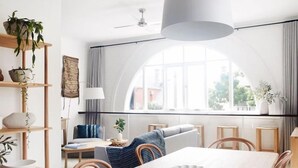 A modern dining area with a wooden table, chairs, and a large window with a view of buildings. - Flourish ON Bull - Stunning New Loft Apartment - Iconic Building  (Newcastle)