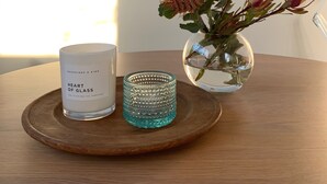 A wooden table with a candle labeled "Heart of Glass," a decorative glass holder, and a vase with flowers. - Inner city garden studio in the heart of Footscray (Footscray)