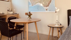 A room with a round wooden table, two black chairs, a small white lamp, and a bed with striped bedding. - Inner city garden studio in the heart of Footscray (Footscray)