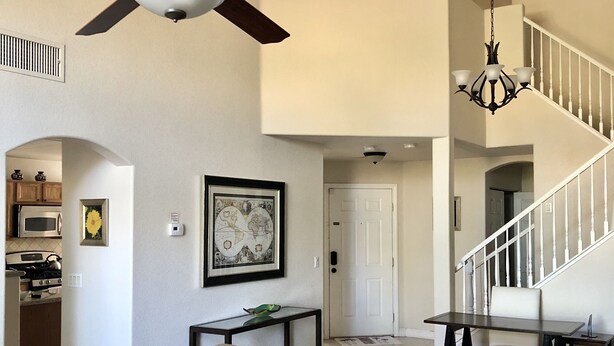 A spacious living room with a ceiling fan, a chandelier, a dining area, and a staircase leading to an upper level.