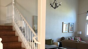 A staircase with white balusters leading to a landing, a chandelier, a sofa set, and a dining table with stools.