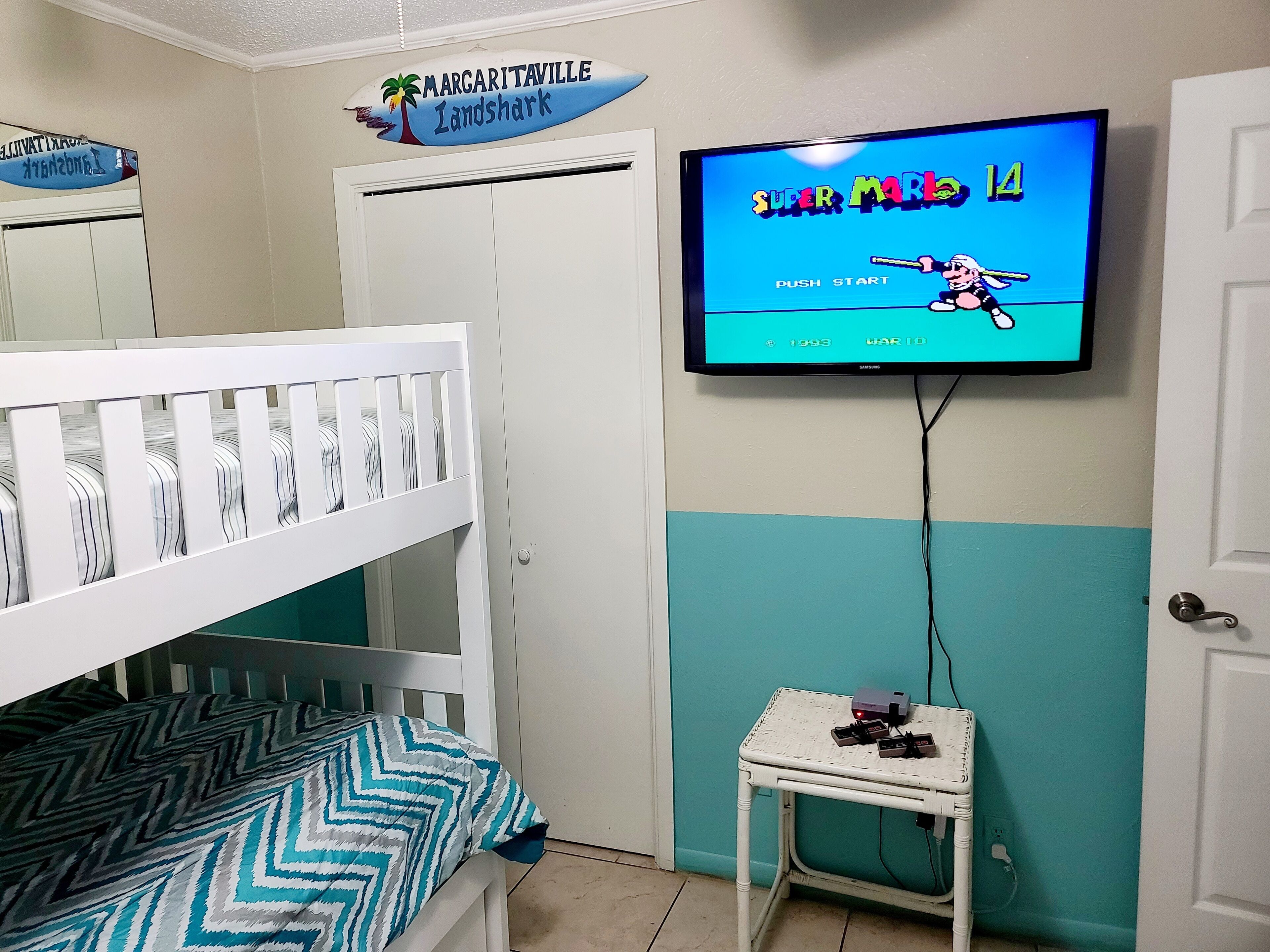 Een slaapkamer met stapelbedden, een televisietoestel waarop een spel wordt getoond, en een klein tafeltje met elektronische apparaten.