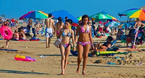 Una playa concurrida, gente caminando y tomando el sol bajo sombrillas de colores.