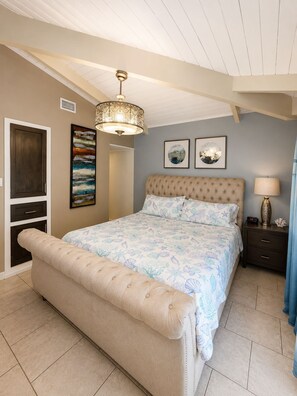 A bedroom with a large bed, a chest of drawers, a bedside table, a lamp, and two wall-mounted pictures.