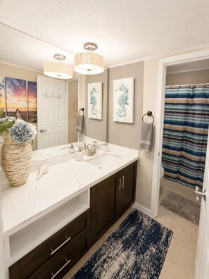 A bathroom with a large white sink, dark wooden cabinets, a blue and white striped shower curtain, and a blue patterned rug.