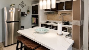A modern kitchen with a stainless steel refrigerator, a white island with bar stools, pendant lights, and a tiled backsplash.