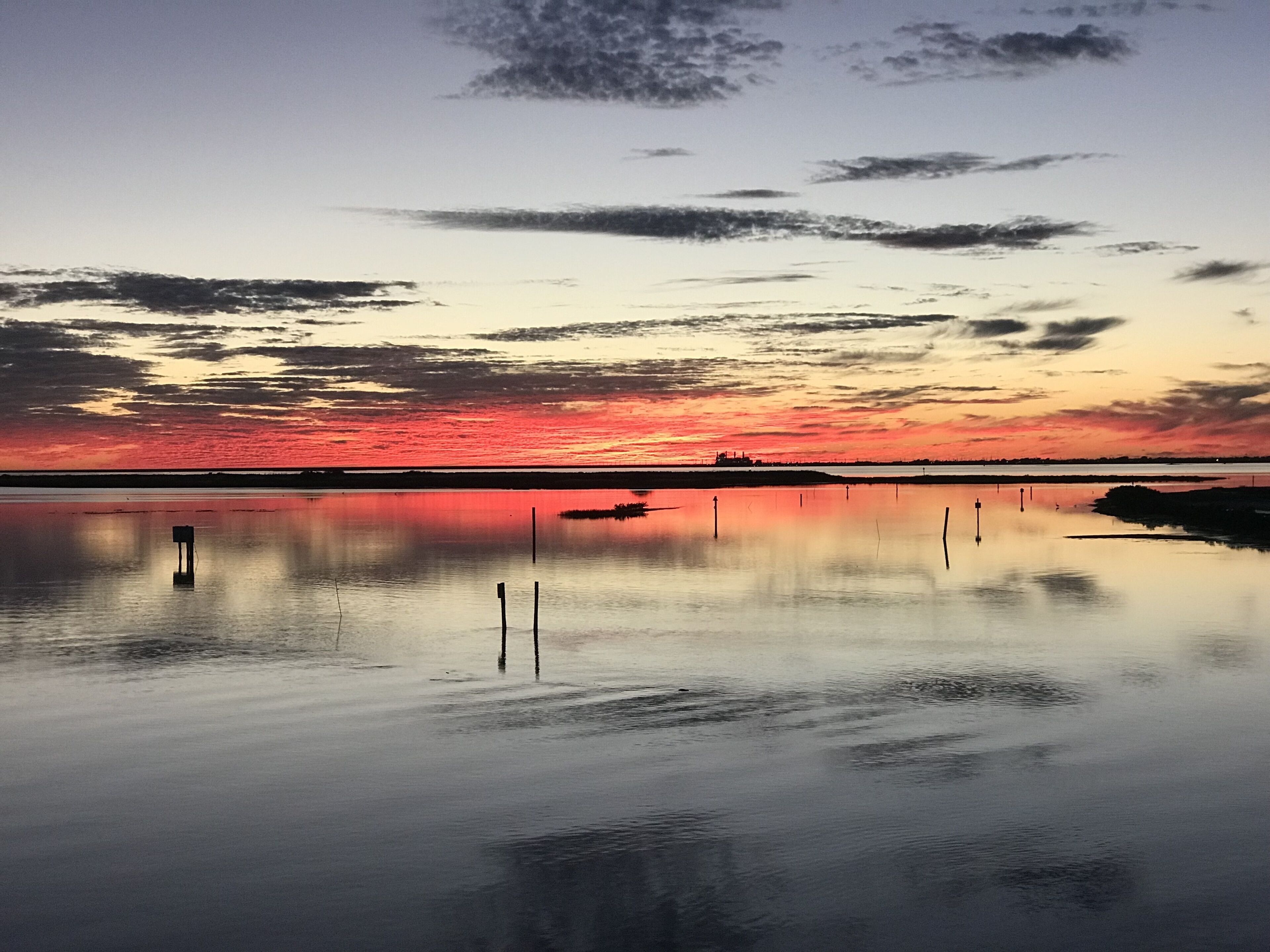 A calm body of water reflecting a sunset sky with clouds.