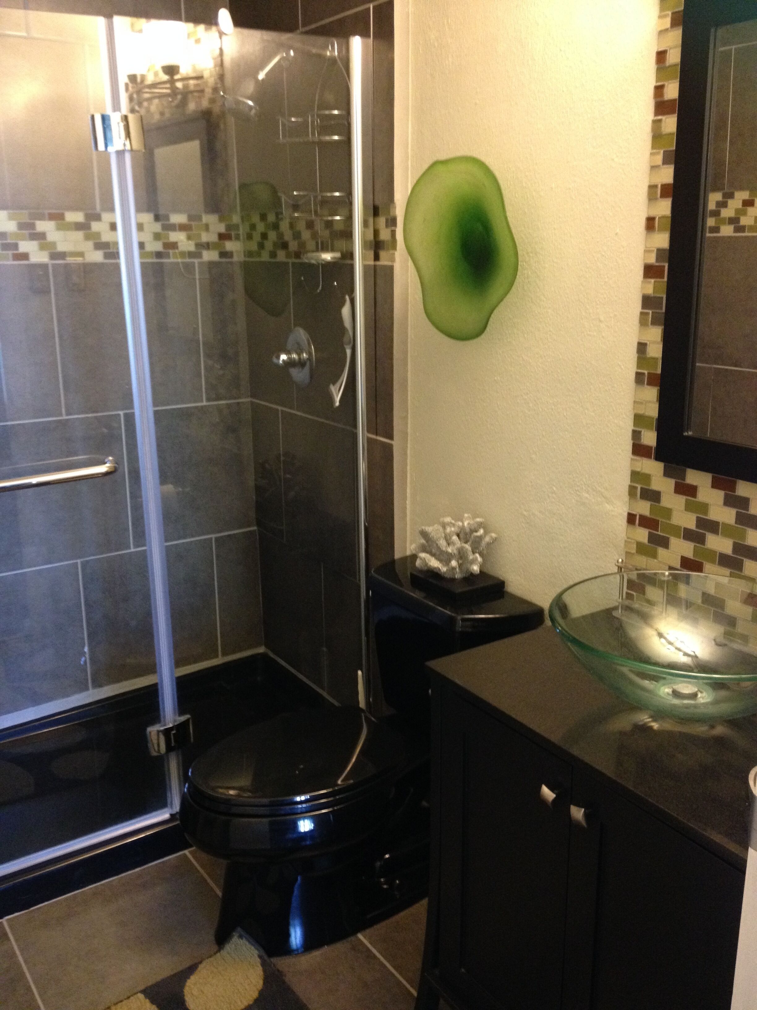 Une salle de bain avec une douche à parois de verre, des toilettes noires et un lavabo en verre.